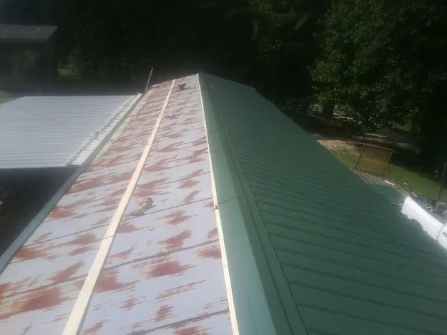 Old rusted panels beside newly installed green metal roofing — Wind Damage Roof Repair by Roofing Brothers in Orleans