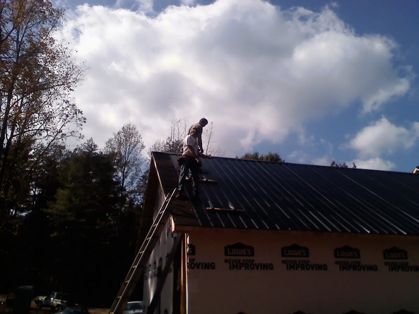 Roofer fastening dark metal panels high against a cloudy sky, from a Roof Inspection job in Orleans